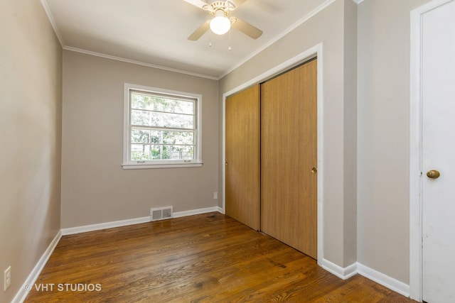 unfurnished bedroom featuring dark wood-style flooring, visible vents, baseboards, a closet, and crown molding