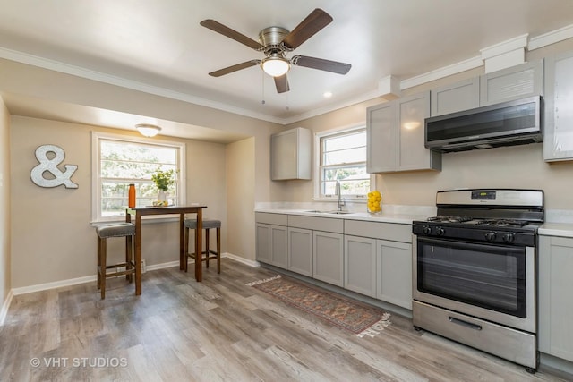 kitchen with gray cabinets, light countertops, light wood-style floors, stainless steel gas stove, and a sink