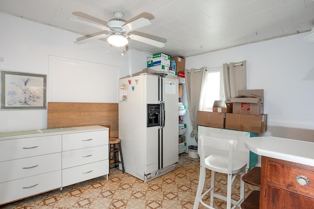 kitchen with light countertops, light floors, white fridge with ice dispenser, and ceiling fan