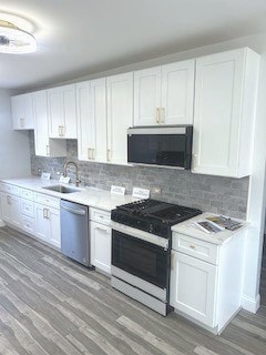 kitchen with wood-type flooring, sink, white cabinetry, and stainless steel appliances