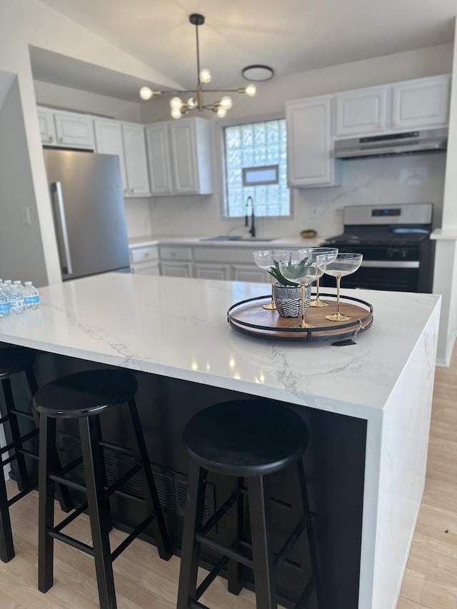 kitchen with white cabinets, light wood-style flooring, stainless steel appliances, under cabinet range hood, and a sink