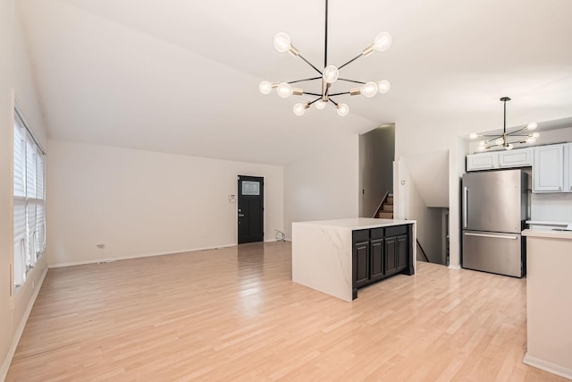 kitchen with white cabinets, stainless steel fridge, light hardwood / wood-style floors, and an inviting chandelier