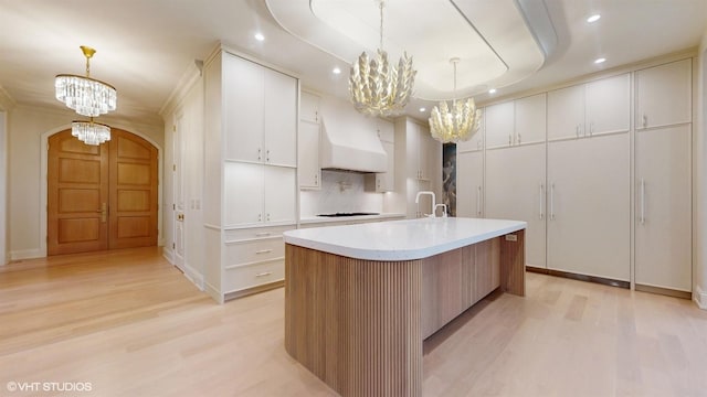 kitchen with premium range hood, white cabinetry, decorative light fixtures, a large island with sink, and a notable chandelier