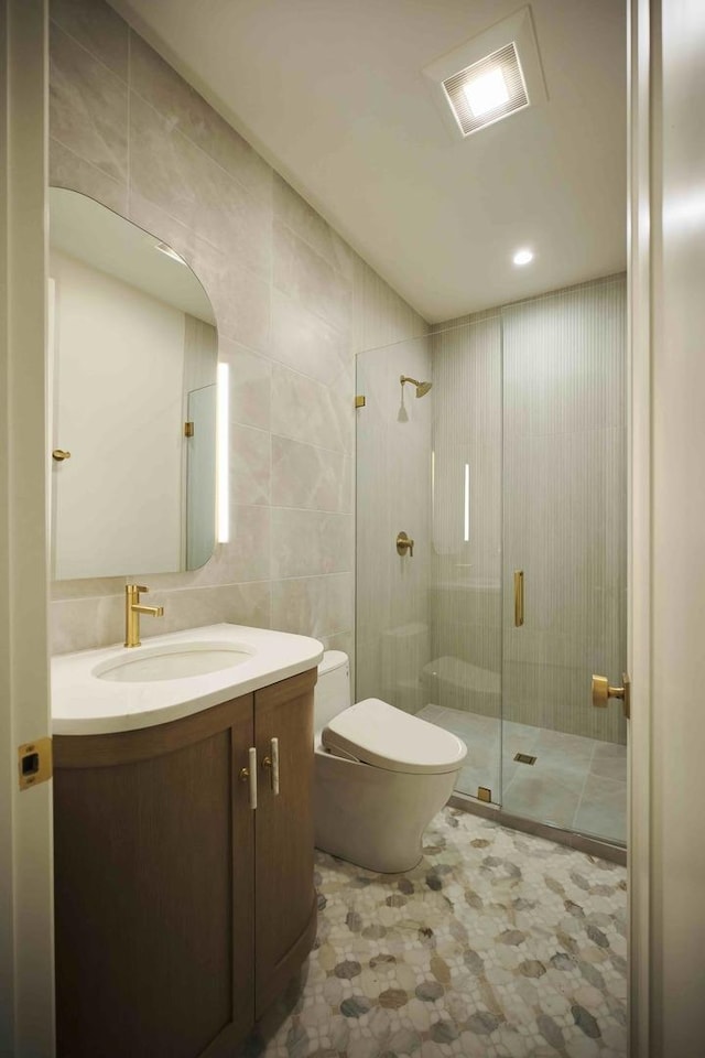 bathroom featuring walk in shower, vanity, toilet, and tile walls