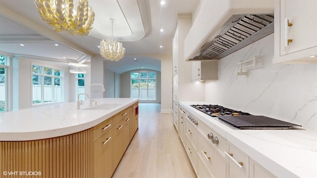 kitchen featuring wall chimney exhaust hood, a kitchen island with sink, hanging light fixtures, and white cabinets