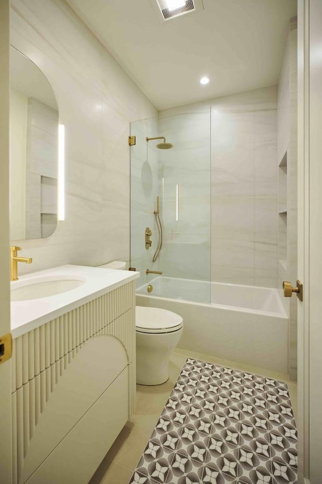 full bathroom featuring tile walls, tile patterned flooring, vanity, tiled shower / bath, and toilet