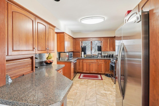 kitchen with backsplash, kitchen peninsula, dark stone counters, and appliances with stainless steel finishes