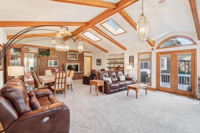 living room featuring beam ceiling, a skylight, french doors, high vaulted ceiling, and carpet floors