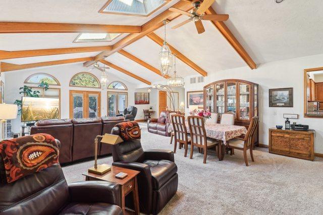 carpeted living room with ceiling fan with notable chandelier and lofted ceiling with beams