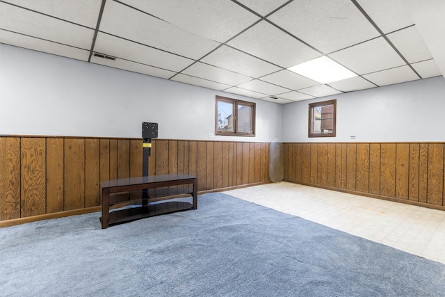 interior space with a paneled ceiling, wood walls, and light colored carpet