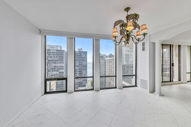 empty room with a chandelier, decorative columns, and a wall of windows