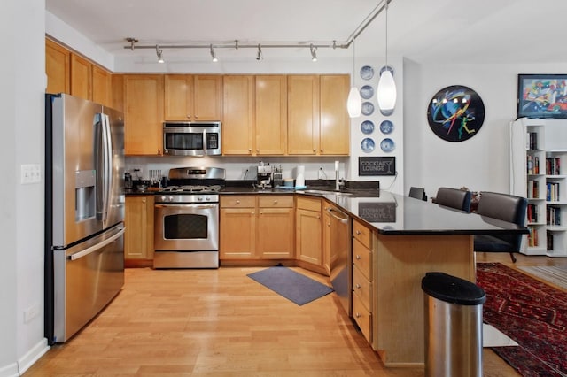 kitchen with light brown cabinets, light hardwood / wood-style flooring, appliances with stainless steel finishes, decorative light fixtures, and kitchen peninsula