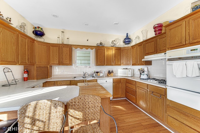 kitchen featuring light wood-type flooring, white appliances, sink, and backsplash