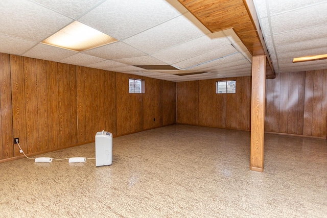 basement with a paneled ceiling, wood walls, and carpet floors