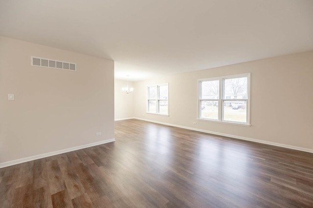 unfurnished room with a notable chandelier and dark wood-type flooring