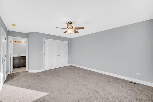 unfurnished bedroom with light colored carpet, a closet, ceiling fan, and connected bathroom