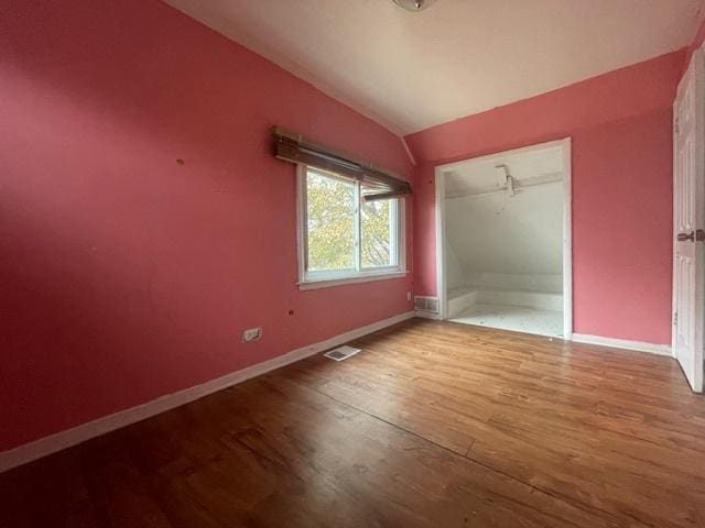 unfurnished bedroom with hardwood / wood-style floors, lofted ceiling, and a closet