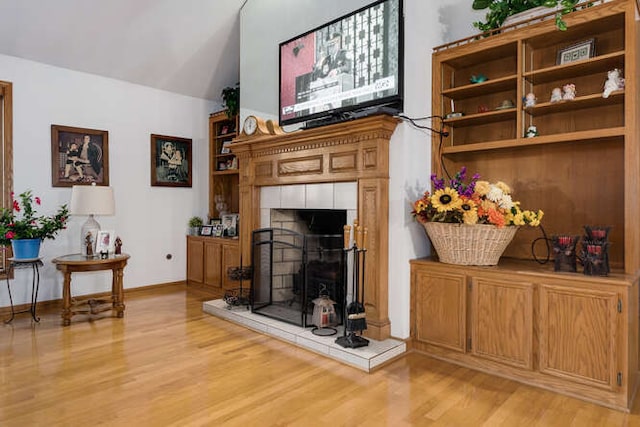 living room featuring vaulted ceiling, light hardwood / wood-style flooring, and a tiled fireplace