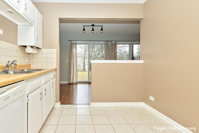 kitchen with white dishwasher, sink, light tile patterned floors, tasteful backsplash, and white cabinetry