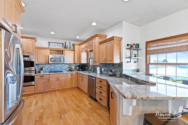 kitchen with a breakfast bar, light wood-type flooring, appliances with stainless steel finishes, light stone counters, and kitchen peninsula