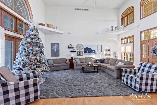 living room with a towering ceiling, hardwood / wood-style flooring, and ceiling fan