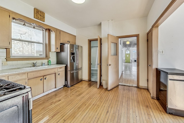 kitchen featuring light hardwood / wood-style floors, stainless steel fridge with ice dispenser, gas range oven, sink, and tasteful backsplash