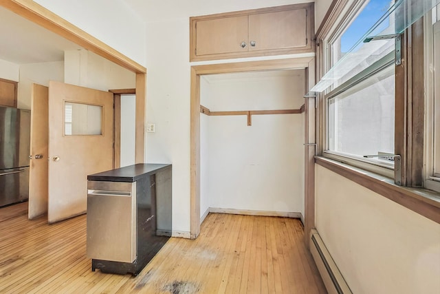 kitchen with a baseboard radiator, light wood-type flooring, a wealth of natural light, and stainless steel refrigerator