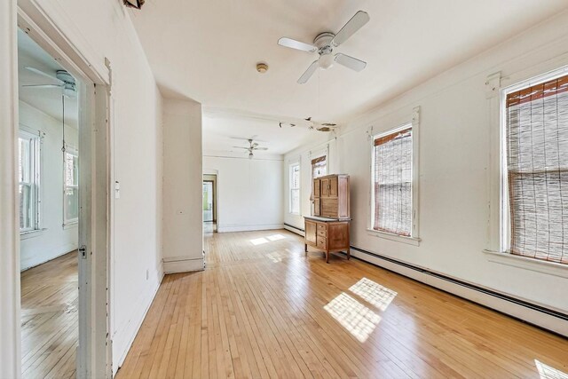 empty room featuring a baseboard heating unit, ceiling fan, and light hardwood / wood-style flooring