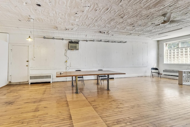 recreation room featuring ceiling fan, a wall unit AC, light hardwood / wood-style floors, and radiator heating unit