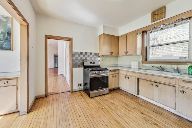 kitchen with sink, light hardwood / wood-style floors, stainless steel gas range, and tasteful backsplash