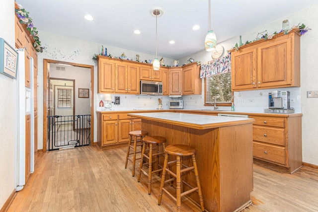 kitchen featuring a breakfast bar, sink, light hardwood / wood-style flooring, decorative light fixtures, and a kitchen island