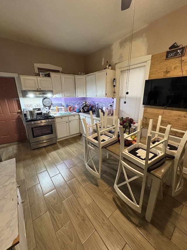 kitchen with pendant lighting, backsplash, white cabinets, light hardwood / wood-style flooring, and stainless steel gas stove