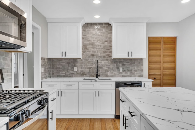 kitchen featuring white cabinetry, sink, stainless steel appliances, light hardwood / wood-style flooring, and backsplash