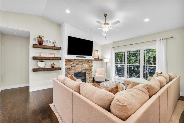 living room featuring ceiling fan, a stone fireplace, lofted ceiling, and dark wood-type flooring