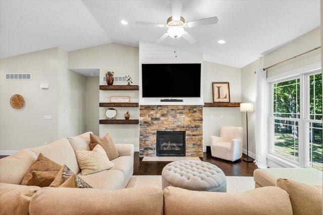 living room with ceiling fan, a stone fireplace, dark wood-type flooring, and vaulted ceiling