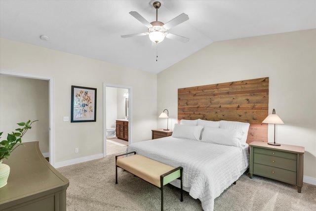 carpeted bedroom with ensuite bath, ceiling fan, and lofted ceiling