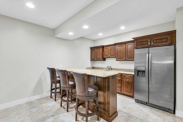 kitchen featuring kitchen peninsula, stainless steel fridge, light stone countertops, and a kitchen breakfast bar