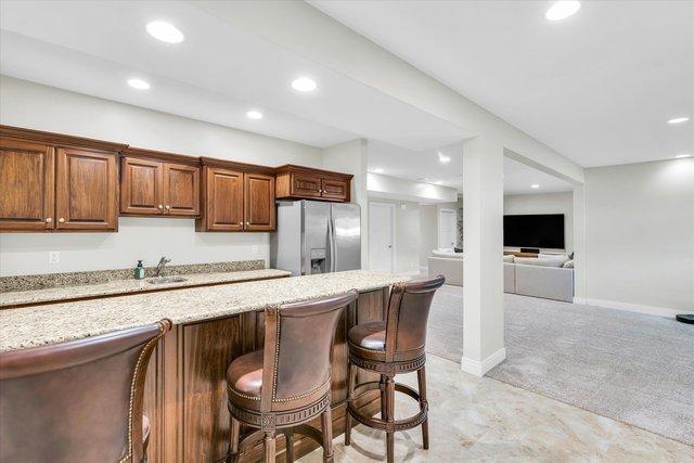 kitchen featuring stainless steel fridge, light colored carpet, light stone countertops, and a breakfast bar area