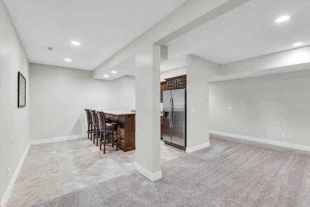 bar with light colored carpet, dark brown cabinetry, and stainless steel refrigerator with ice dispenser