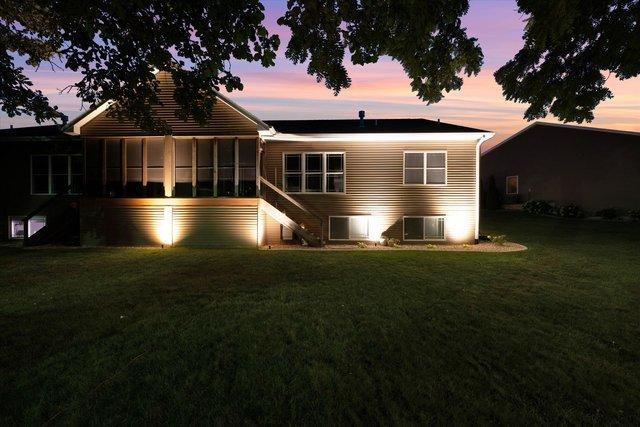 back house at dusk with a lawn, central air condition unit, and a sunroom