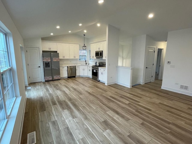 kitchen with appliances with stainless steel finishes, decorative light fixtures, light hardwood / wood-style flooring, white cabinetry, and lofted ceiling