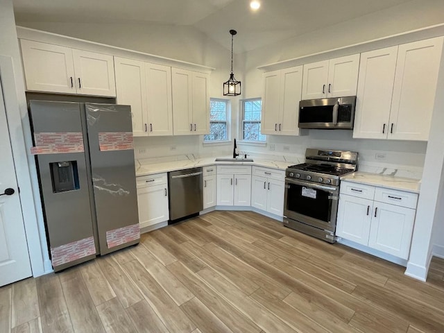 kitchen with light wood-type flooring, stainless steel appliances, vaulted ceiling, white cabinetry, and hanging light fixtures