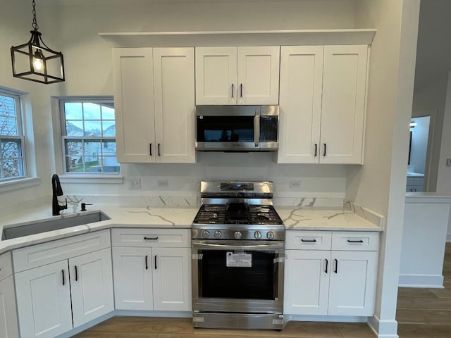 kitchen featuring light stone countertops, stainless steel appliances, sink, pendant lighting, and white cabinets