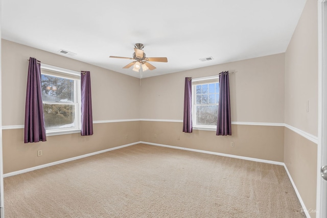 carpeted empty room with baseboards, visible vents, and a ceiling fan