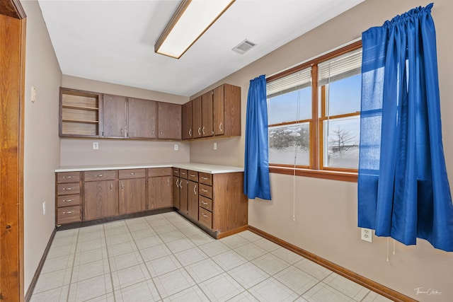 kitchen with baseboards, brown cabinetry, visible vents, light countertops, and open shelves