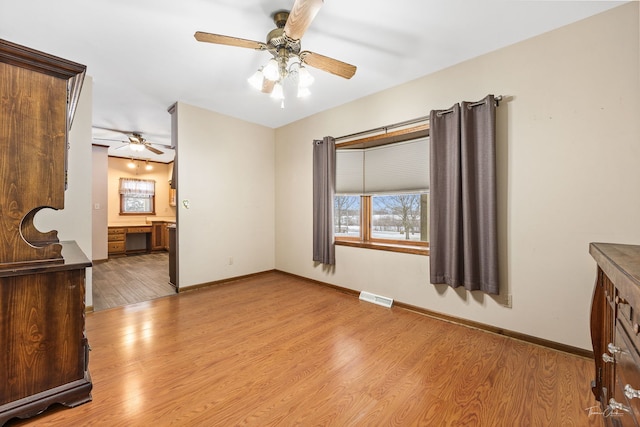 empty room featuring light wood finished floors, a ceiling fan, visible vents, and baseboards