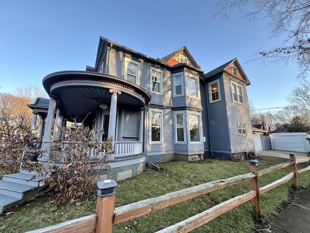 victorian house featuring a garage, covered porch, an outbuilding, and a front yard