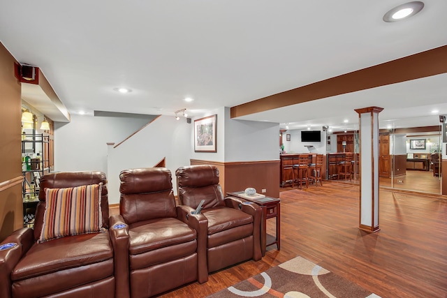 cinema room with hardwood / wood-style floors, wood walls, bar, and decorative columns