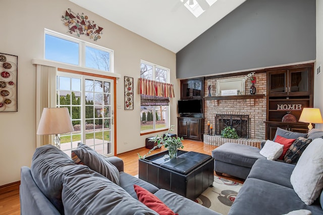 living room with a fireplace, high vaulted ceiling, a skylight, and light hardwood / wood-style flooring