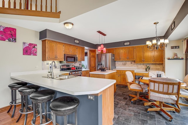 kitchen featuring kitchen peninsula, appliances with stainless steel finishes, a kitchen bar, sink, and an inviting chandelier